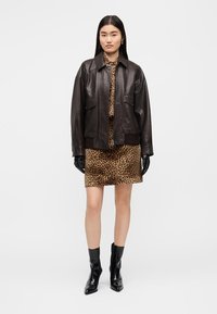 Chaqueta de cuero negra con múltiples bolsillos, usada sobre un vestido con estampado de leopardo. Guantes negros y botines brillantes completan el conjunto.