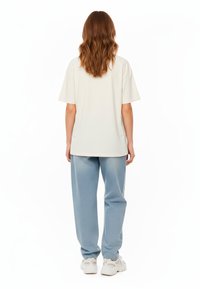T-shirt oversize beige chiaro abbinato a jeans larghi blu chiaro. La t-shirt ha maniche corte e i jeans presentano un leggero effetto lavato.