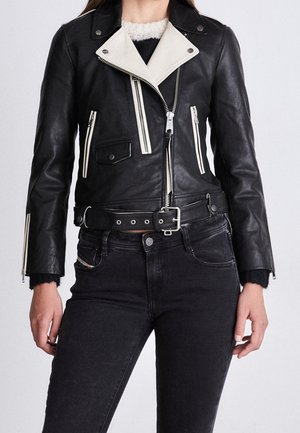 Zwarte leren motorjack met witte kraag, zilveren ritsen en zakken. Gemaakt over een zwarte sweater en gecombineerd met donkere jeans.