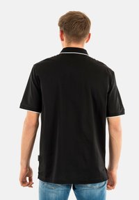 Polo nero con colletto corto, rifiniture bianche sul colletto e sulle maniche, realizzato in un tessuto morbido, indossato con jeans blu.