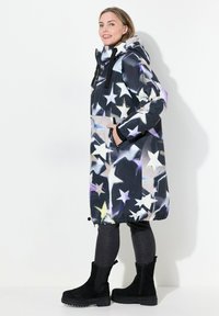 Svart parkas med stjärnmönster i vitt, lila och blått. Har dragsko i nederkant, huva och framfickor. Bärs över mörka jeans och svarta kängor.