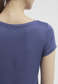 Lila kortärmad skjorta med rund halsringning och mjuk, slät textur, med synliga sömmar nära halsringningen.