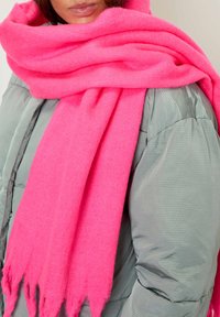 Person wearing a bright pink thick scarf wrapped around neck and shoulders over a light gray padded jacket.