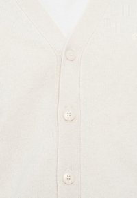 Lys beige strikket cardigan med dyp V-hals, med fire runde knapper og et teksturert mønster på stoffet.