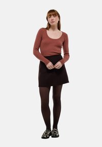 Haut à manches longues marron côtelé et mini-jupe noire. Modèle portant des collants transparents marron et des chaussures slip-on à motifs. Design simple et ajusté.