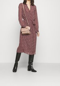 Bordeaux blommig klänning med långa ärmar och knytmidja, bärs med knähöga svarta stövlar. En liten beige axelväska ger kontrast.