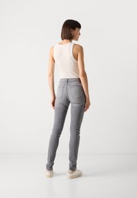 Grå slim fit jeans med middellang livhøyde og detaljerte baklommer. Kombinert med en hvit singlet og lys fottøy.