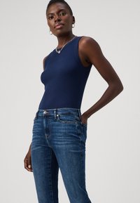 Marineblå ribbestrikket tanktop kombinert med tilpassede blå jeans som har subtile slitasjedetaljer og kobberfarget hardware. Enkelt, klassisk design.