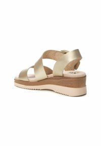 Sandalia de cuero dorado con tiras entrecruzadas, tacón de madera y suela de goma beige clara. Plantilla texturizada para mayor comodidad.