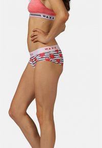 Culotte pour femmes à rayures blanches et noires, avec des motifs de cœurs rouges. Taille élastique avec le logo "WAXX" en rouge. Texture de tissu doux.