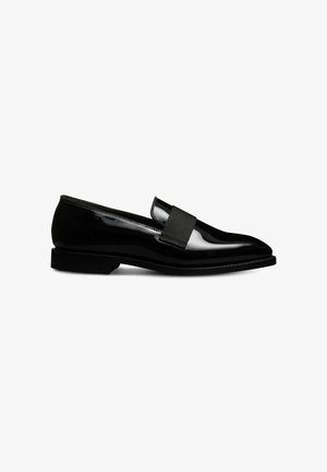 Mocassins en cuir verni noir avec une semelle plate, un bout pointu et un détail de sangle élastique sur le cou-de-pied. Fini lisse et brillant.