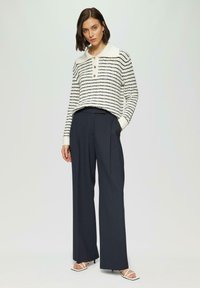 Pull en tricot rayé avec un design blanc et marine, doté d'un col polo et de trois boutons. Associé à un pantalon large marine sur mesure.