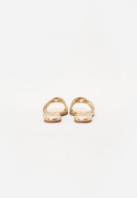 Gullfargede flate sandaler med kryssende stropper og en glatt, skinnende overflate. Åpen tå-design og flat såle med minimalistisk estetikk.
