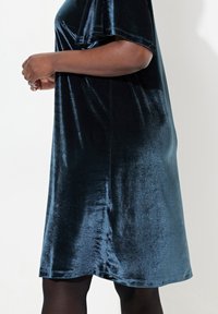 Tummansininen samettimekko lyhyillä hihoilla ja rentoa istuvuutta, jossa on sileä pinta ja polvimittainen helma.