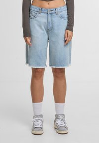 Persona que lleva unos pantalones cortos de mezclilla azul claros hasta la rodilla con dobladillos deshilachados, calcetas blancas, zapatillas grises y una camiseta de manga larga gris.