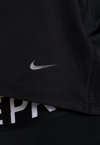 Černý sportovní top s pozitivním stříbrným logem Nike na hrudi a viditelným černým pasem s bílým písmem, zvýrazňující elegantní design a texturu látky.