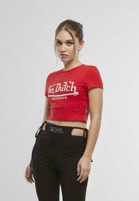 Červené zkrácené tričko s bílým logem "Von Dutch". Spárováno s černými kalhotami s výřezy a kamínkovými akcenty na pase.