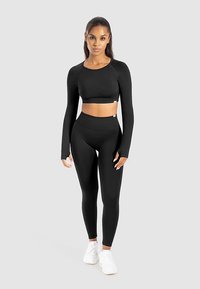 Sort langærmet croptop og højtaljede leggings lavet af strækstof, kombineret med hvide sneakers. Glat tekstur, tætsiddende design.