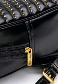 Czarna skórzana torebka z złotymi ćwiekami, wyposażona w złoty suwak z etykietą "WITTCHEN" i teksturowanym, pikowanym wzorem.
