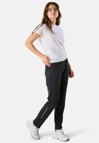 Grå idrottsbyxor med sidofickor och en rosa logotyp, tillsammans med en vit t-shirt med kort ärm och vita sneakers.