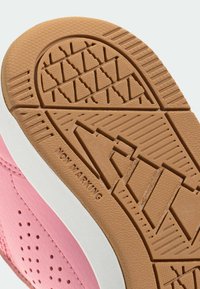 Różowy trampek z cholewką z teksturowanej skóry, białą środkową podeszwą oraz brązową gumową podeszwą zewnętrzną z bieżnikiem niepozostawiającym śladów.