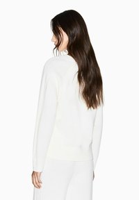 Weißer Strickpullover mit geripptem Saum und Bündchen. Hat eine lockere Passform und strukturierte Details an den Schultern. Glatte, weiche Textur.