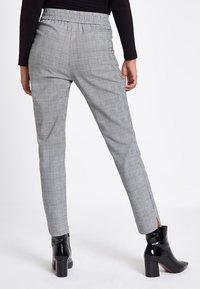 Grå rutiga byxor med elastisk midja, smal passform och sidoöppningar vid fållen. Bärs med svarta lackade ankelstövlar.