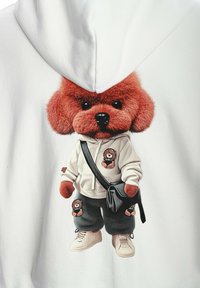 Sudadera blanca con un perro rojo de estilo cartoon y suave, que lleva un logo de osito, combinada con pantalones negros y zapatillas beige.