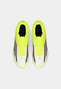 Κίτρινα και λευκά αθλητικά παπούτσια με υφή στην επάνω μεριά, που διαθέτουν μαύρες ρίγες και κορδόνια. Σχεδιασμένα για απόδοση με αεροδυναμικό σχήμα.