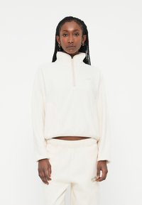 White fleece pullover with a high collar and half-zip design. Features side pockets and a relaxed fit, paired with matching sweatpants.