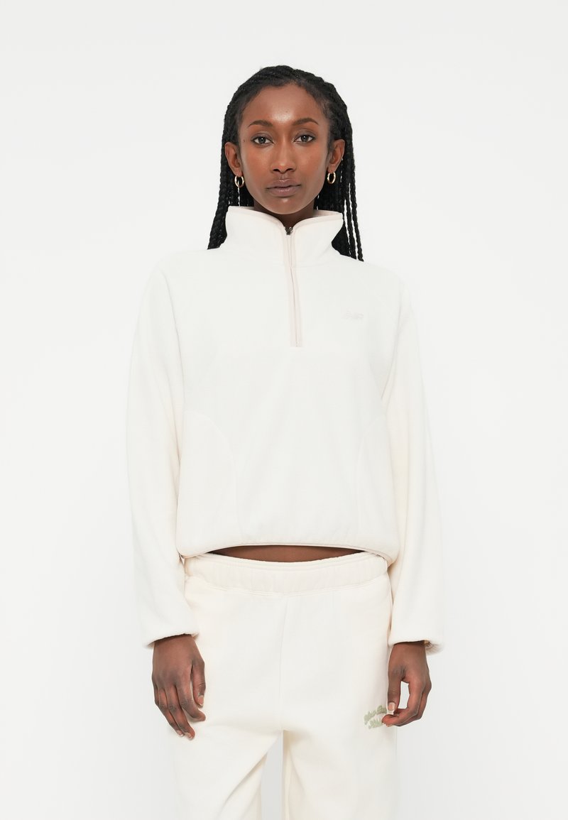 White fleece pullover with a high collar and half-zip design. Features side pockets and a relaxed fit, paired with matching sweatpants.