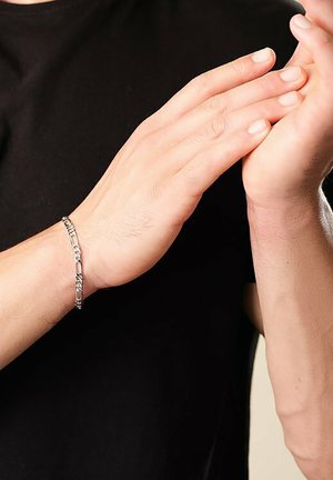 Silberne Kettenarmband mit ineinandergreifenden Gliedern, am Handgelenk getragen. Glatte Textur, minimalistisches Design und glänzendes Finish auf einem schwarzen Hemd.