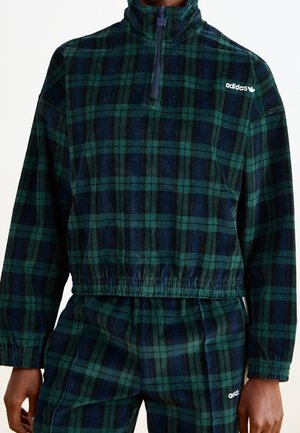 Zielono-granatowa koszulka na długi rękaw z krótkim zamkiem, w kratę, z logo Adidas na piersi, noszona z dopasowanymi spodniami.