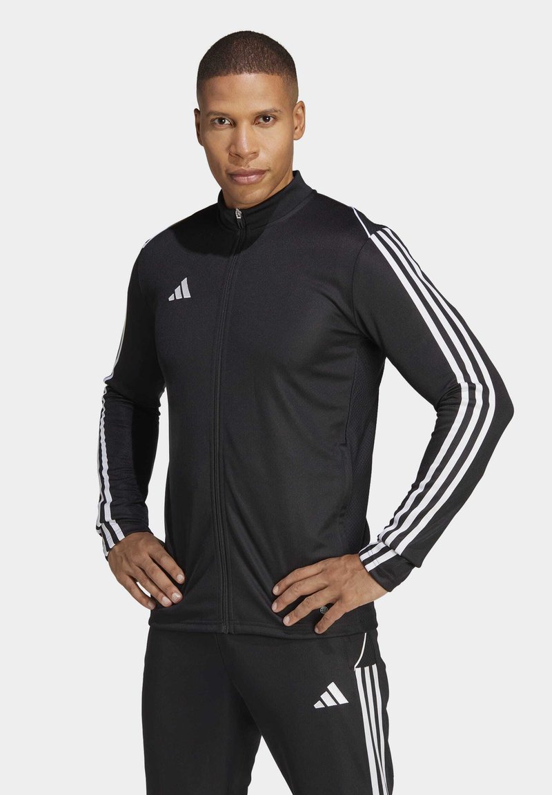 Must musta jakk, kõrge krae, täispikk tõmblukk ja valged triibud varrukatel; sisaldab Adidas logo rinnal ja varrukal.