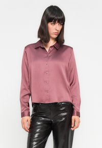 Satijnen, mauve blouse met een puntkraag, knoopsluiting aan de voorkant en lange mouwen, gecombineerd met glanzende zwarte pantalons.