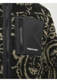 Fleecová bunda s černým a krémovým vířivým vzorem. Obsahuje černou zipovou kapsu s logem 'Originals Studio'. Texturovaný, útulný materiál.