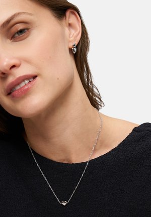 Silbernes Herz-Collier an einer zarten Kette, kombiniert mit silbernen Ohrringen in Blattform. Die Oberfläche ist glatt und das Design ist elegant.