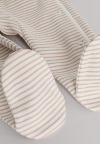 Soft beige and white striped baby footed pajamas with snap buttons, shown close-up on a light surface.