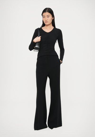 Μαύρη μακρυμάνικη μπλούζα με ρέλια στη μέση, συνδυασμένη με ψηλόμεσο, φαρδύ μαύρο παντελόνι. Ομοιόμορφο, απαλό ύφασμα σε όλο το ένδυμα.
