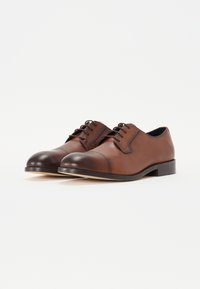 Scarpe eleganti in pelle marrone con punta arrotondata, design stringato e punte in una tonalità più scura in contrasto. Suole piatte e semplici dettagli di cucitura.