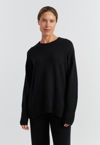 Schwarzer Strickpullover mit Rundhalsausschnitt, gerippten Bündchen und Saum. Besitzt eine lockere Passform und weichen Stoff, kombiniert mit passenden schwarzen Hosen.