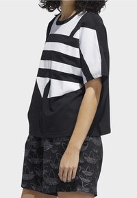 Svart och vit oversized t-shirt med djärva horisontella ränder, tillsammans med svarta shorts med ett texturerat blommönster.