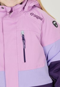 Lila und fliederfarbene isolierte Jacke mit einer Reißverschlusstasche, verstellbarer Kapuze und gesticktem Logo auf der Schulter. Glatte Textur und sportliches Design.