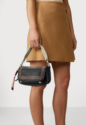 Schwarze Ledertasche mit bunten Nähten und einem geflochtenen Griff, ausgestattet mit dekorativen Akzenten und einem Verschluss.