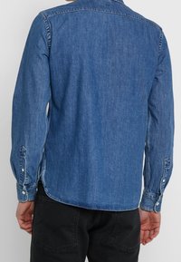 Denim overhemd met lange mouwen, een kraag, knoopmanchetten en een vervaagde blauwe afwerking; afgeronde zoom met zijsplitten en een gestructureerde stof.