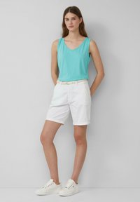 Helles blaues ärmelloses Top mit einem V-Ausschnitt, kombiniert mit weißen knielangen Shorts und weißen Sneakers. Das Outfit ist einfach und lässig.