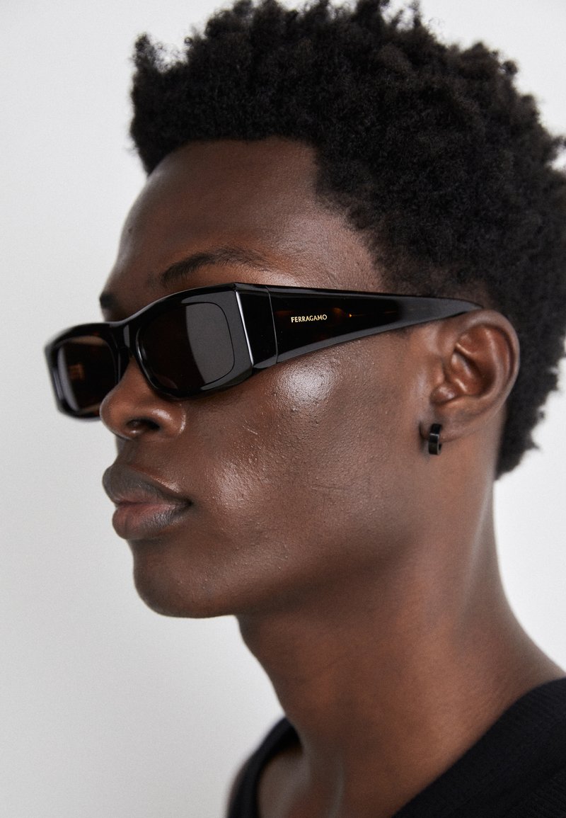 Black rectangular sunglasses with thick frames and dark lenses, featuring the "Ferragamo" logo. Textured finish on the frames.