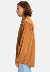 Bruine corduroyshirt met een kraag, borstzak en lange mouwen. Heeft een iets losse pasvorm en een gestructureerde stof.
