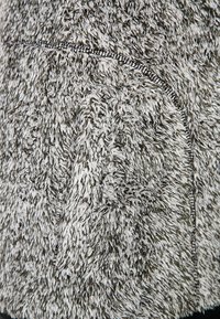 Gros plan sur un tissu polaire gris et blanc texturé avec une couture en point overlock noir visible le long d'une couture courbe.