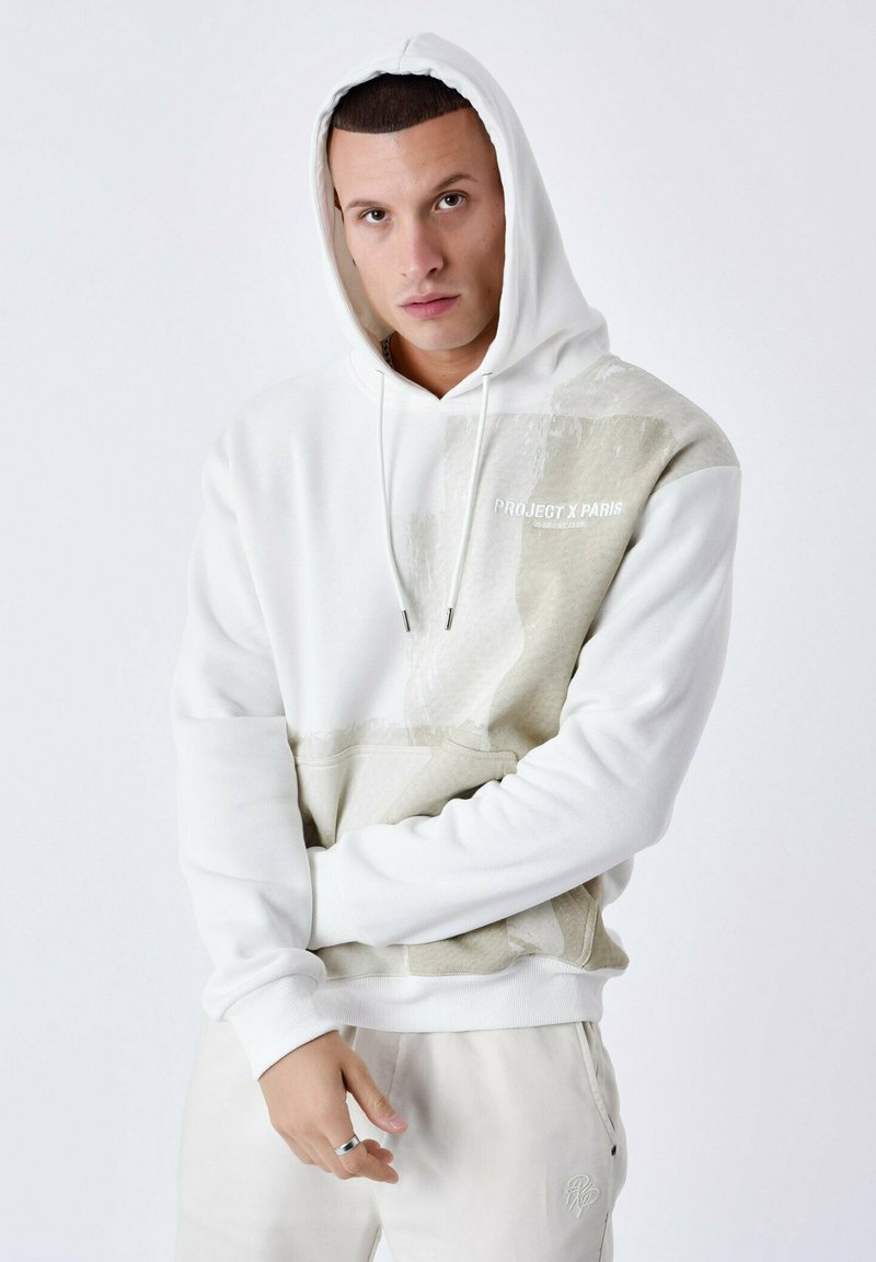 Sudadera blanca con capucha, con un parche texturizado en beige, un bolsillo frontal y cordones. Presenta el texto del logo "PROJECT X PARIS" en el pecho.